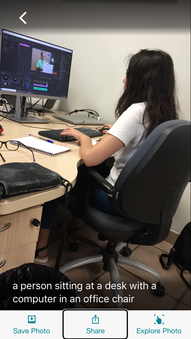 Fotografía de una mujer sentada delante de un ordenador con un texto que describe la escena reconocida por la aplicación